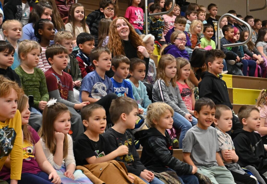 A auditorium full of excited elementary school students sit and watch a performance.