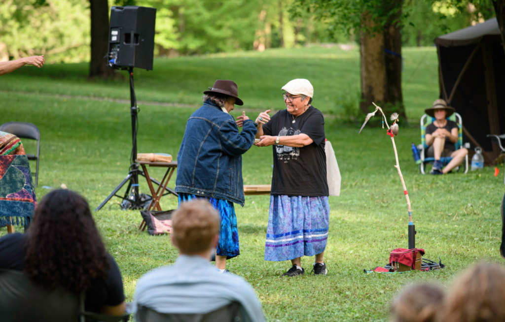 Two people perform on the lawn as part of The Missouri River Water Walk in May 2021. People sit in lawn chairs in a circle around them and watch.
