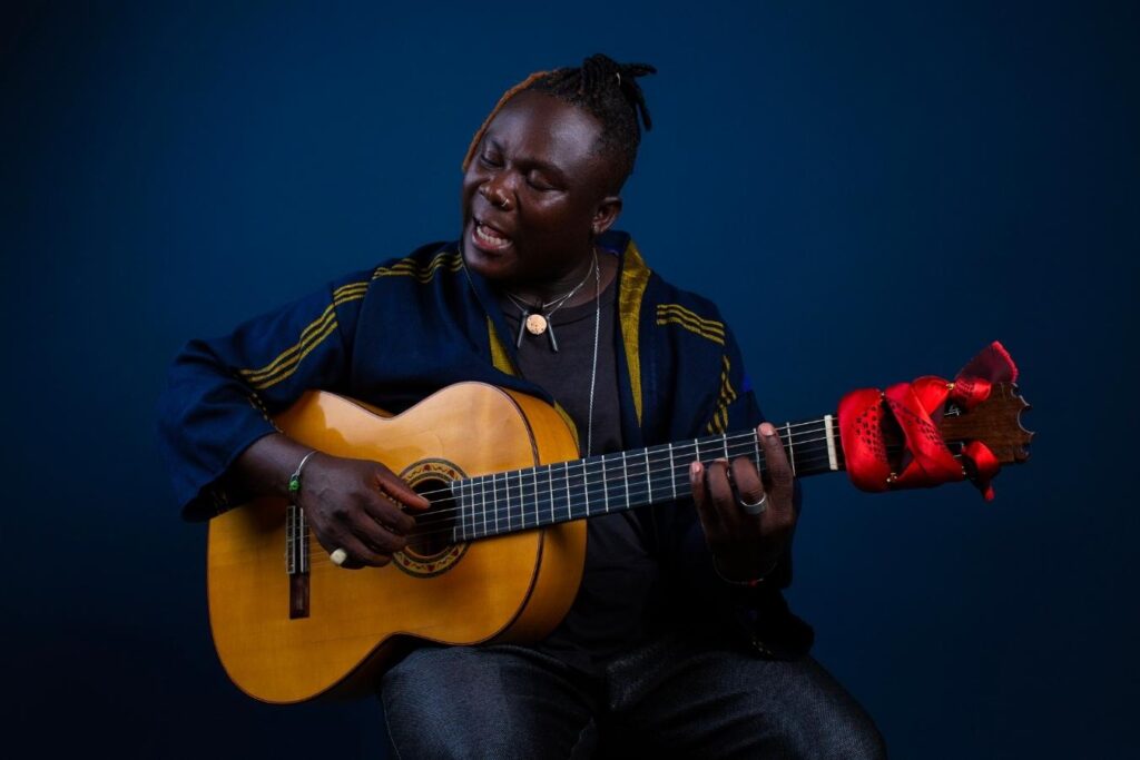 Okaidja Afroso, an artist from Ghana, sits while playing guitar and singing.