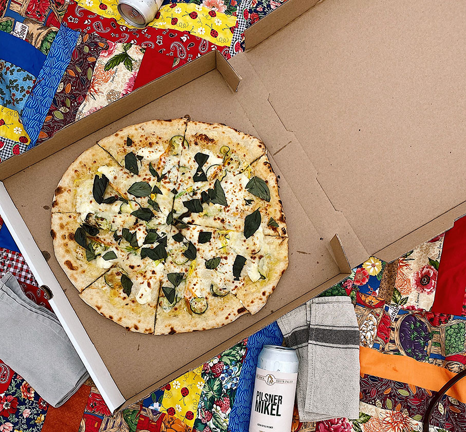 Pizza in a cardboard takeout box sits on top of a patchwork quilt