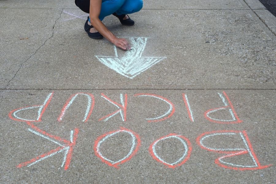 A person draws an arrow in chalk on the sidewalk, below the words "book pickup."