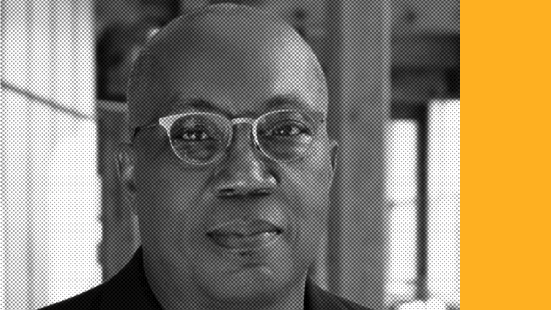 Headshot of a smiling person of dark skin tone, who is bald and wearing light framed glasses.