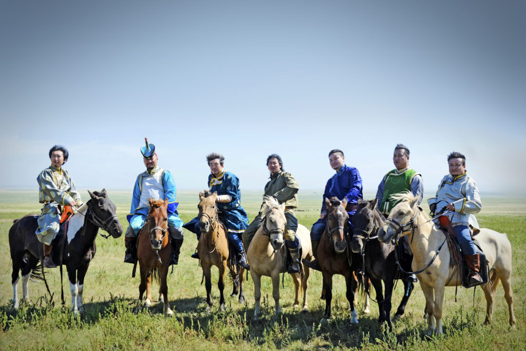 Choor, a Mongolian music band based in China, are posed in a line sitting on top of horses in the countryside.