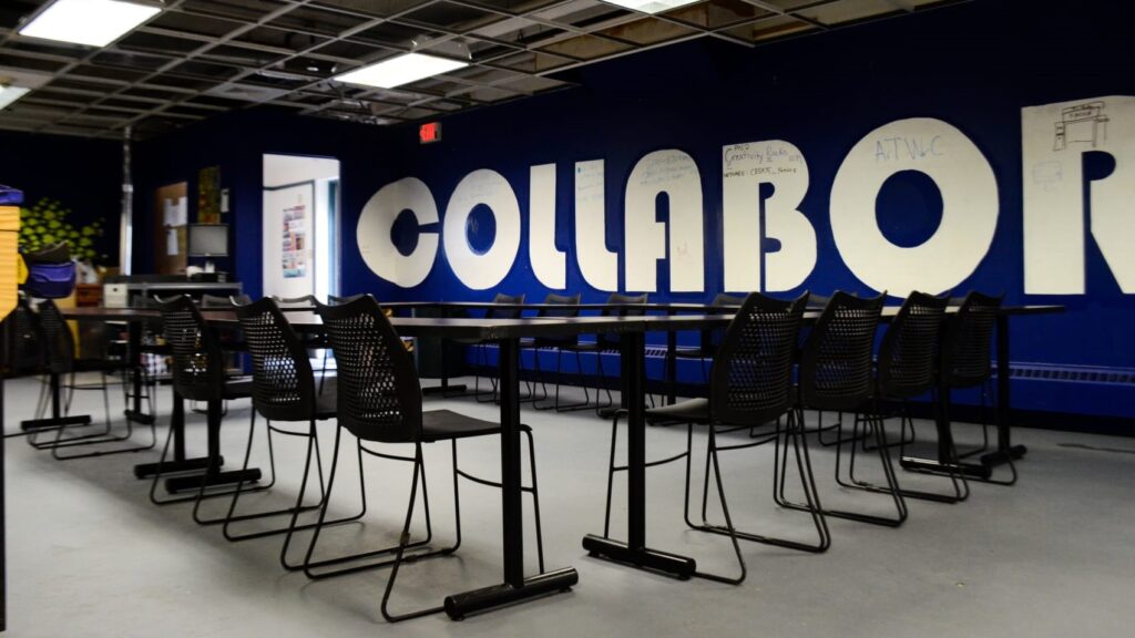 A table with chairs around it, in front of wall that reads "Collaborate" in giant letters.