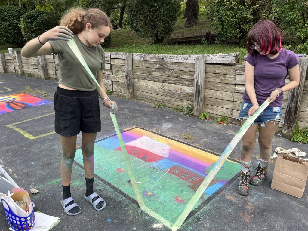 Students from Rosboro Middle School and Heights High School youth group peel the tape off around a colorful chalk drawing.
