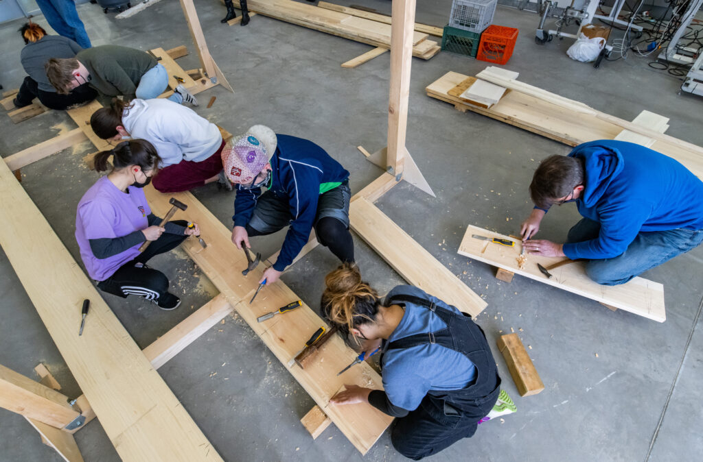 Students use hammers and chisels to carve dovetails keys into the base of the boat as Douglas Brooks' traditional Japanese wooden boatbuilding apprentices.