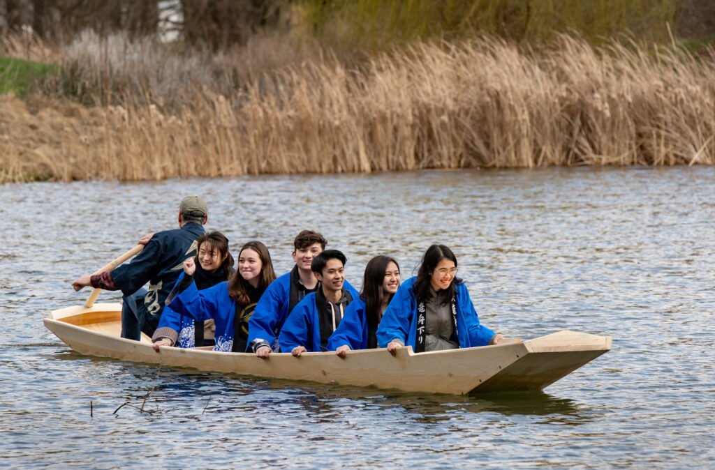 A group of students smile as they ride in a Japanese river boat on the water.