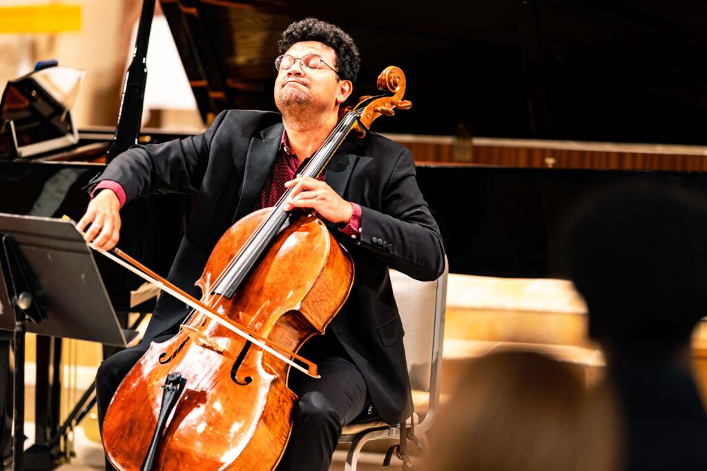 A person sits in a chair on a stage playing a cello.