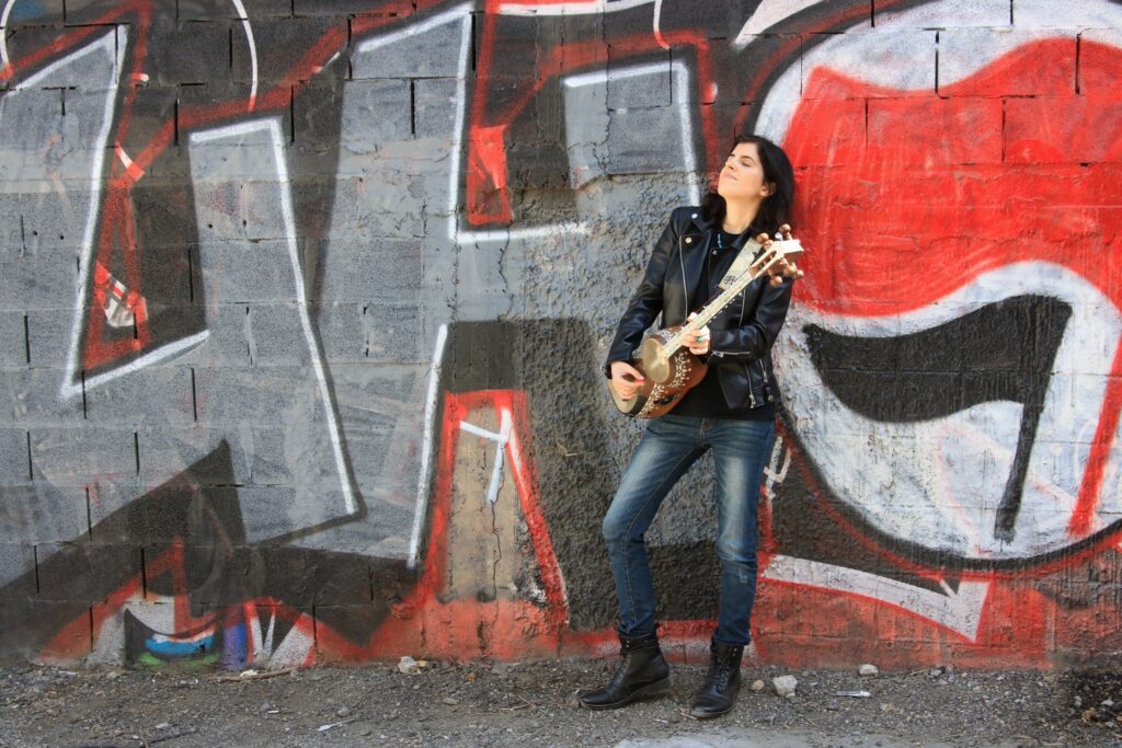 Hadar Maoz, an artist based in Israel who finds inspiration from sounds from ancient Persia to modern Israel, poses with an instrument against a wall with graffiti art.