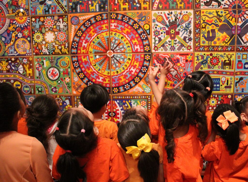 Pre-COVID-19, students take in a Huichol mural called “The New Awakening.” There are approximately 1,523,520 hand-laid beads in this work of art.