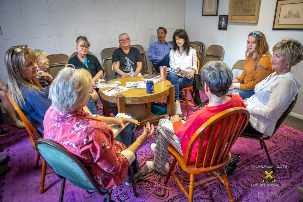 People sitting in chairs gathered in a circle, in discussion and with books in their hands.