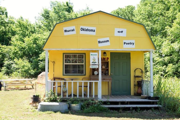 A small yellow house with a green door, with the words "Rural Oklahoma Museum of Poetry" posted near the roof.