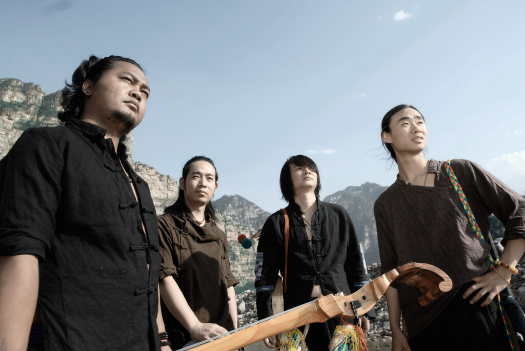 Shanren, a folk-fusion band based in China, pose together while looking off into the distance. There's a mountain range in the background.