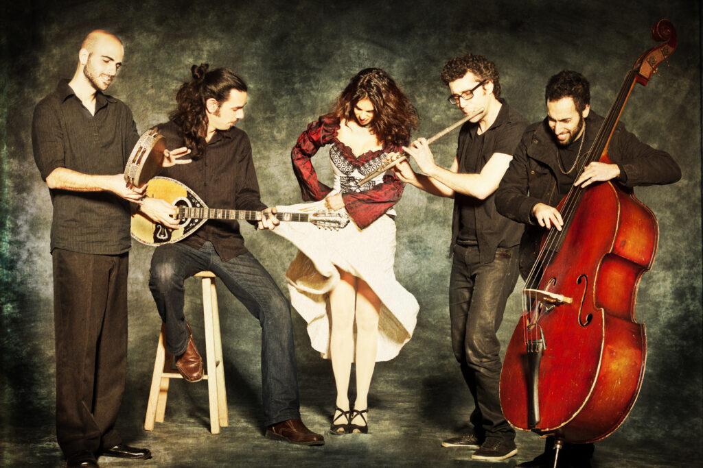 Yamma Ensemble, a band based in Israel, pose with various instruments including a standing bass and tambourine.