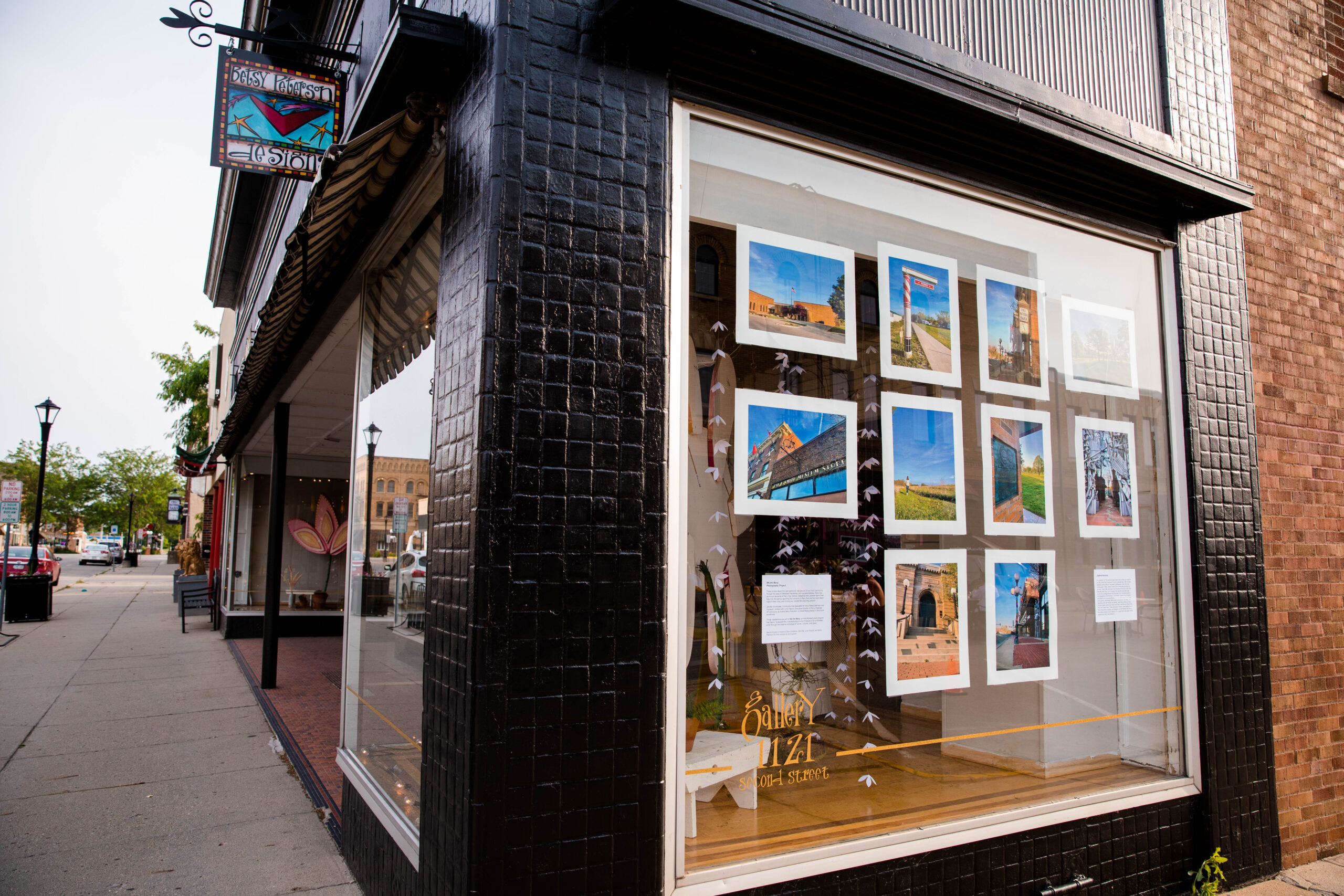 Photographs hang on the window of an art gallery with a shop sign labeled "Betsy Peterson Design."