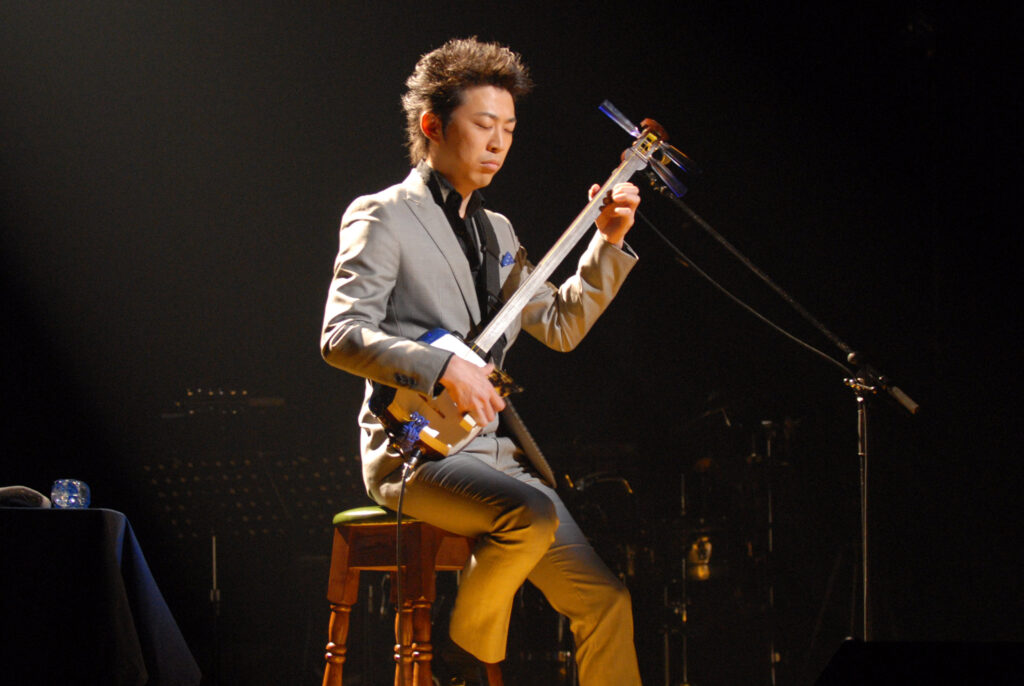Agatsuma, an artist based in Japan and known throughout the world for his masterful playing of the tsugaru-shamisen, performs while sitting on a stool onstage.