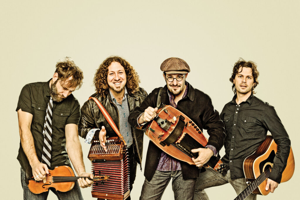 Le Vent Du Nord, a progressive folk band from Québec, poses with their instruments, including a guitar, accordion, and fiddle.