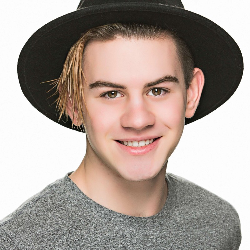 Headshot of a smiling person of light skin tone and short dark blonde hair, wearing a black hat and grey shirt.