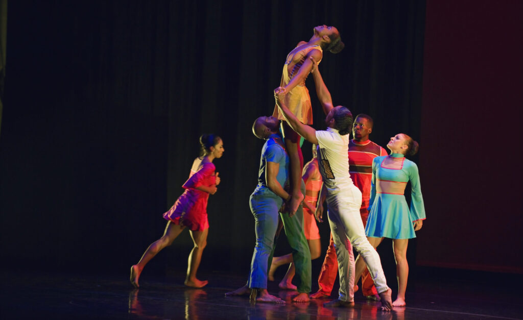 A group of dancers circles around two of them holding one up in the air.