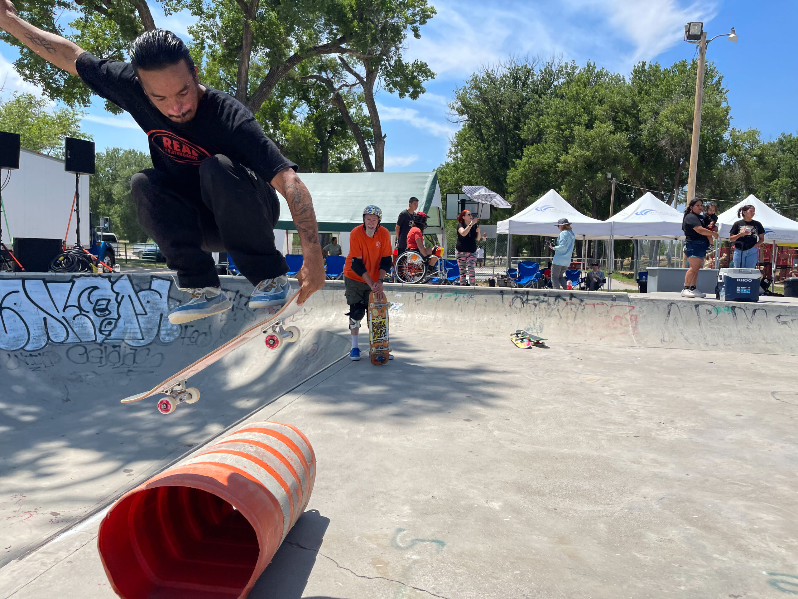 An adult skateboarder jumps over an orange construction cone on its side at a cement skatepark in the Pine Ridge Reservation, home of the Oglala Sioux Tribe in southwest South Dakota.