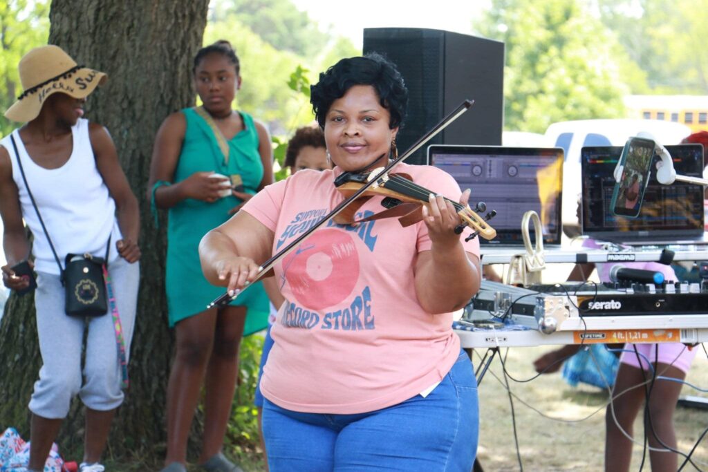 A black woman plays the violin for an onlooking crowd.
