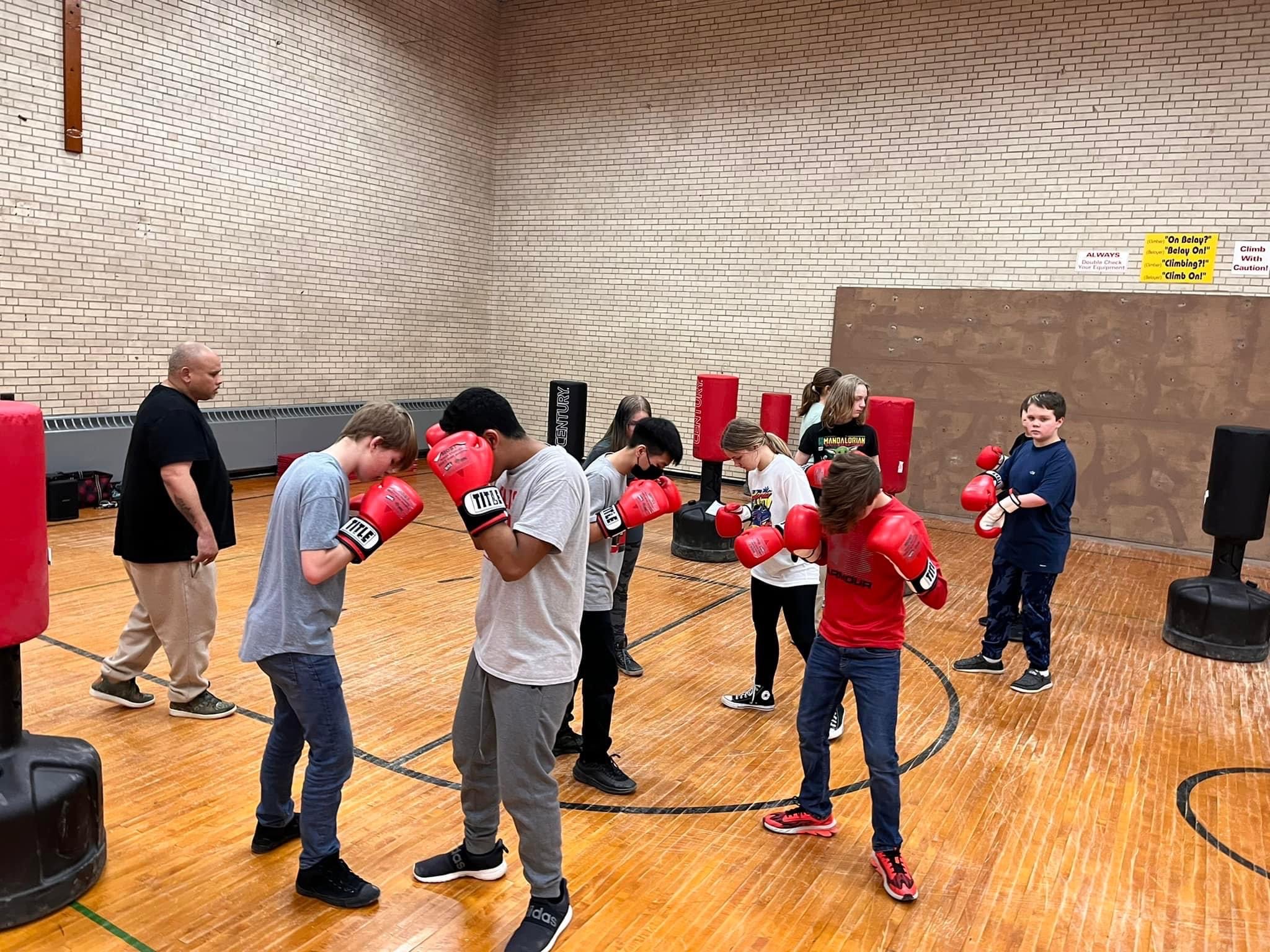 Children paired up in a gym with boxing gloves and punching bags.