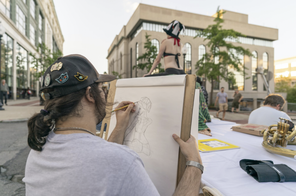 An artist sketching a person posing in the background.