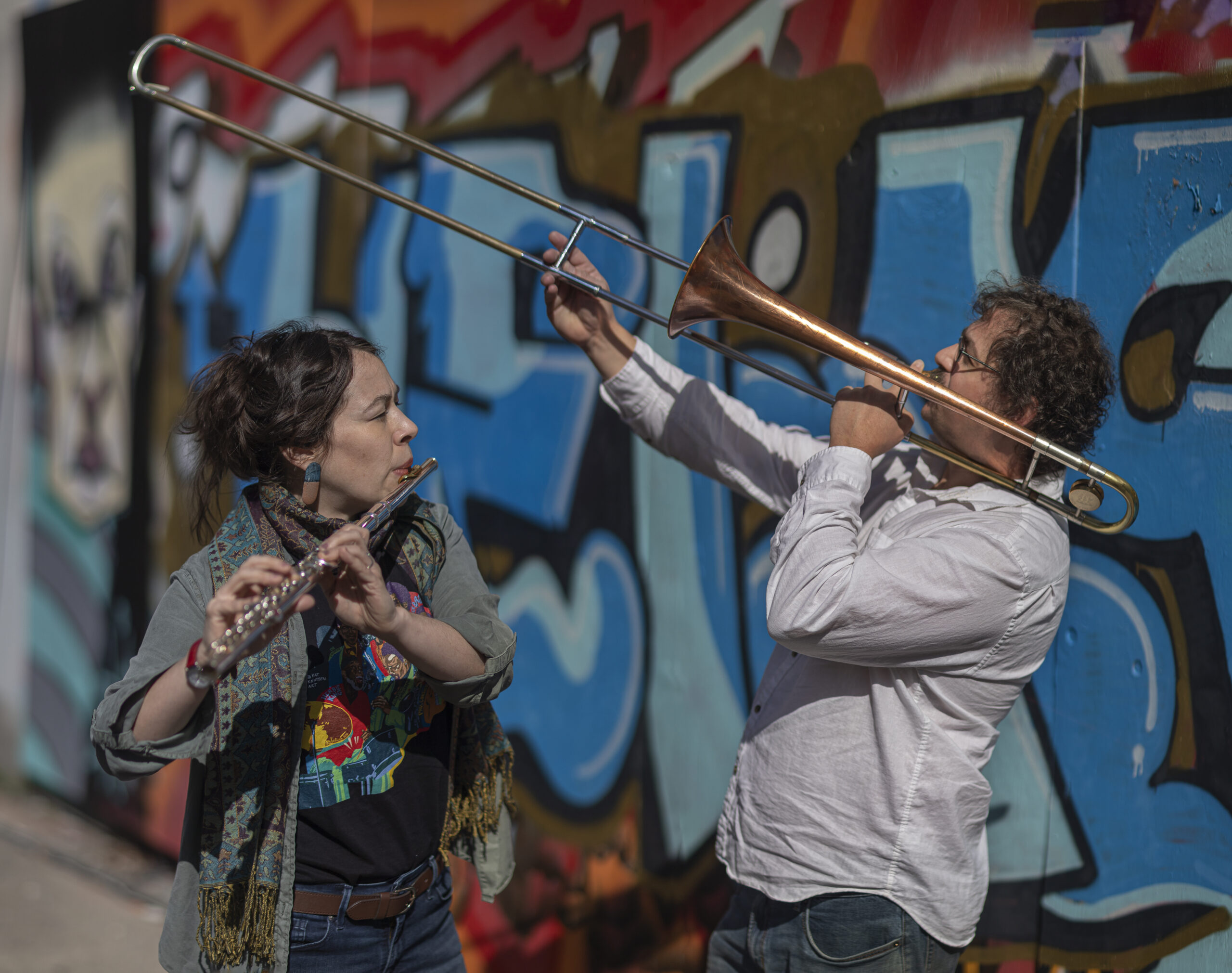 A flautist and trombonist performing in front of a mural.