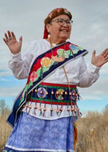 A smiling Native woman with glasses in regalia