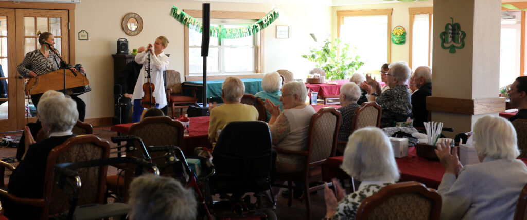 A band performs at a senior center full of older adults who watch the performance attentively