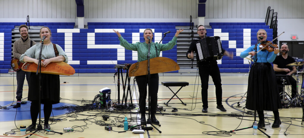 A five piece band performs in a school gymnasium