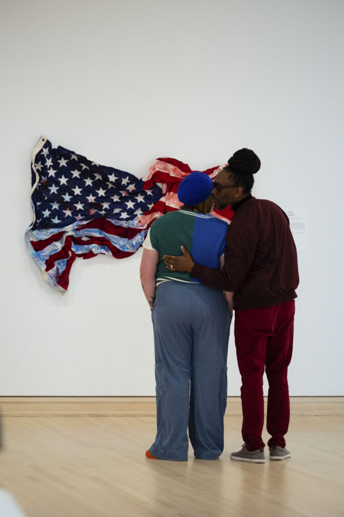 Two attendees look at a painting of a crumpled American flag.