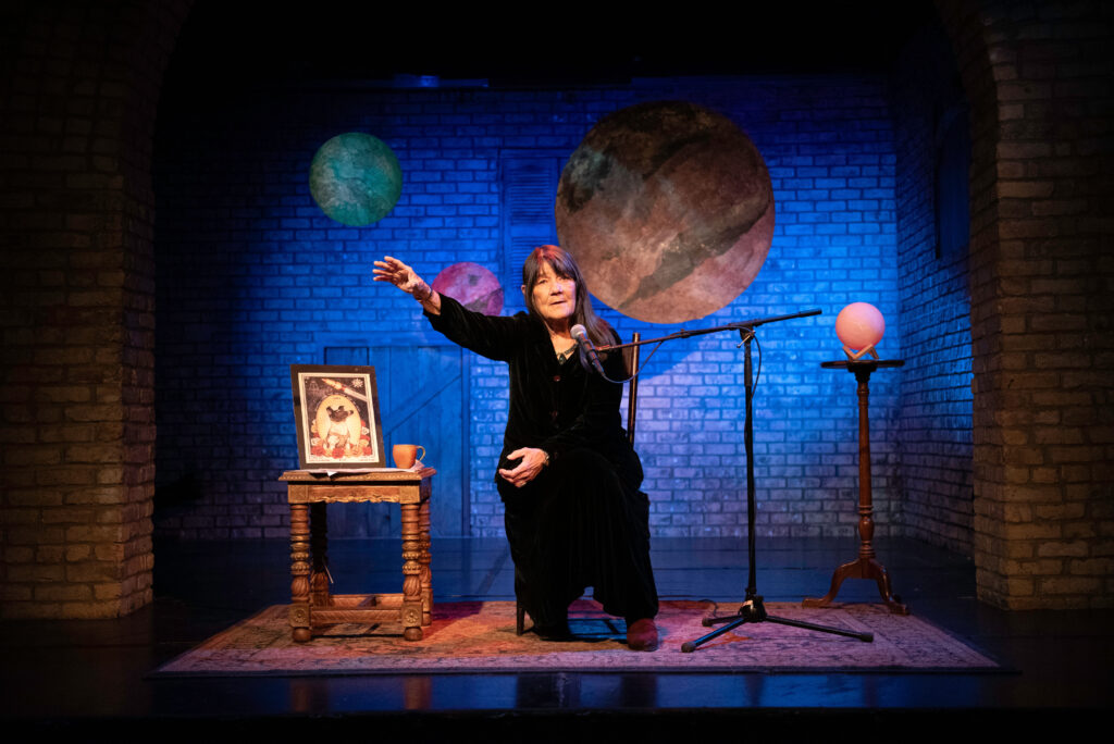 A woman sits on a stage bathed in blue-purple light telling a story.