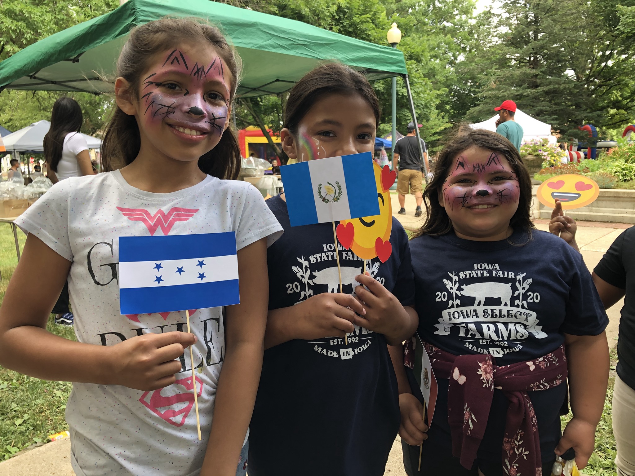 Three young people with facepaint and flags smile for the camera