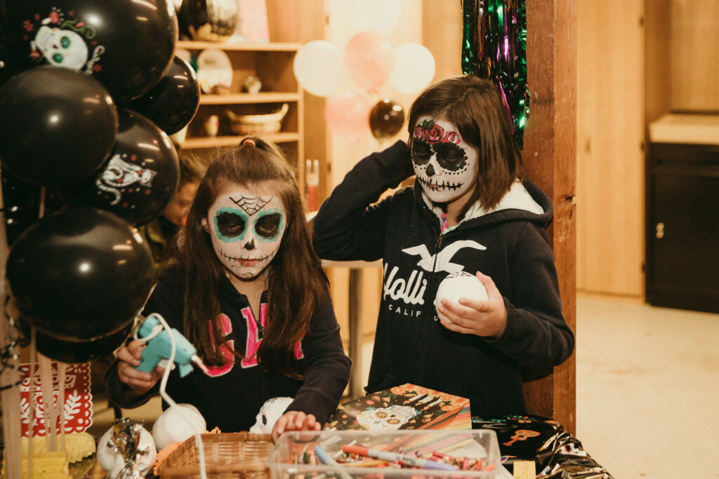 Two girls in sugar skull makeup hold glue guns