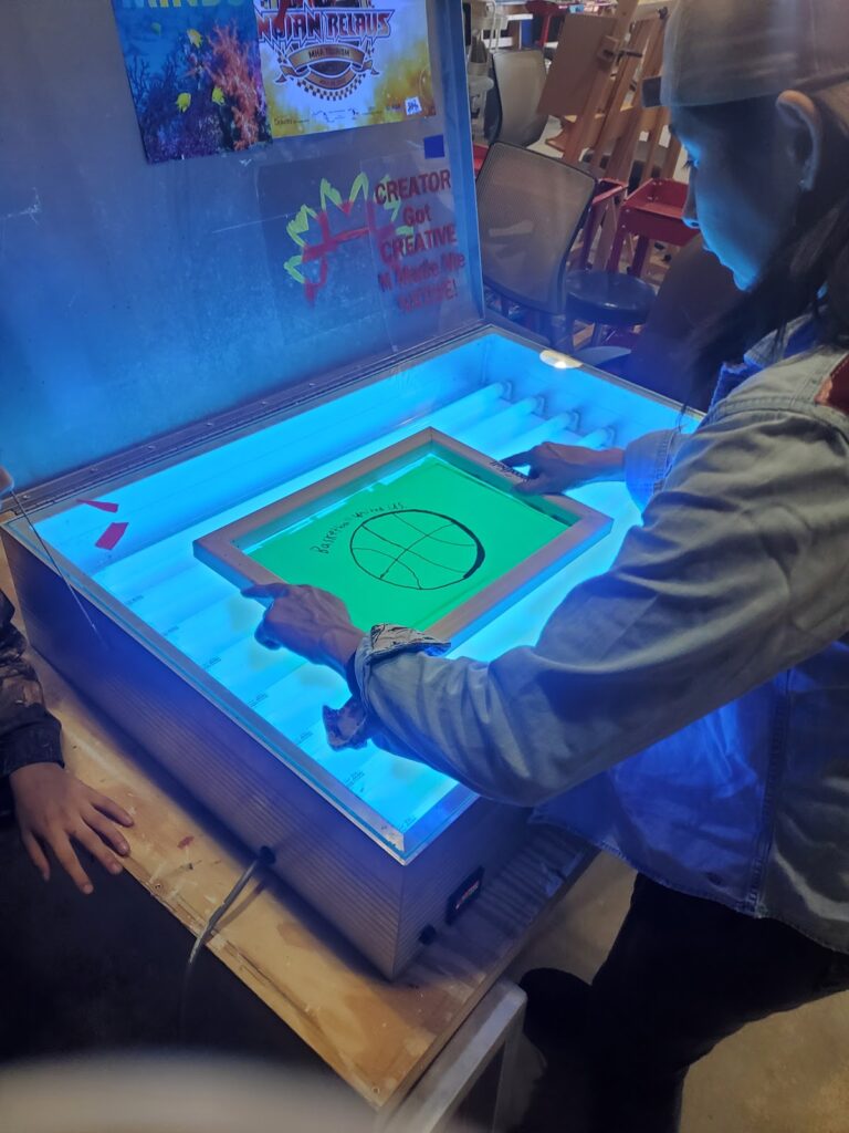 A student uses a lightbox to transfer a design onto a screen printing screen.