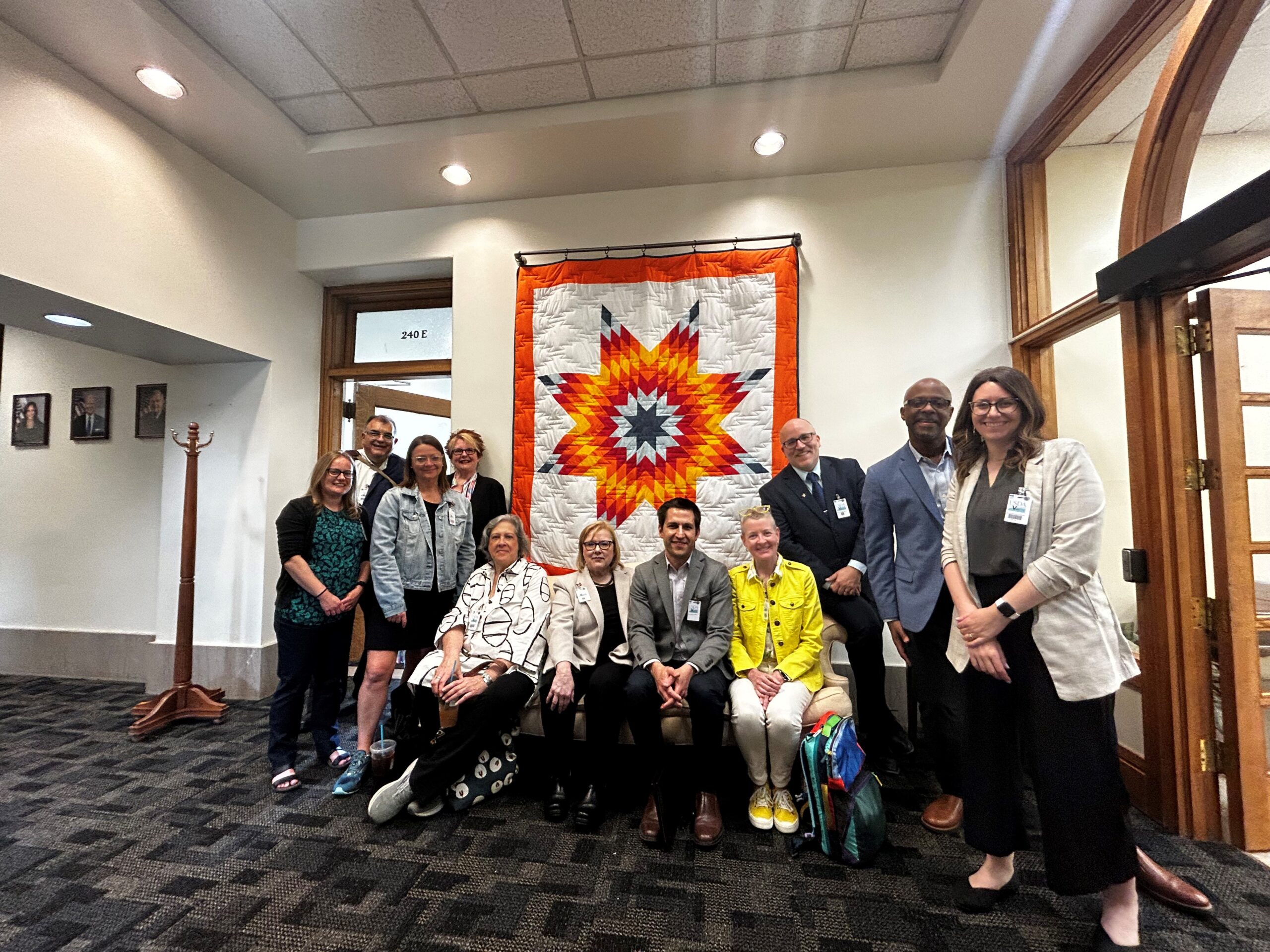 A group of arts leaders in formal wear pose in an office in front of a star quilt