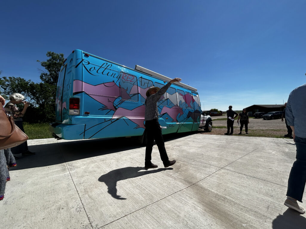 A man stands in front of a colorful van that reads Rolling Rez Arts