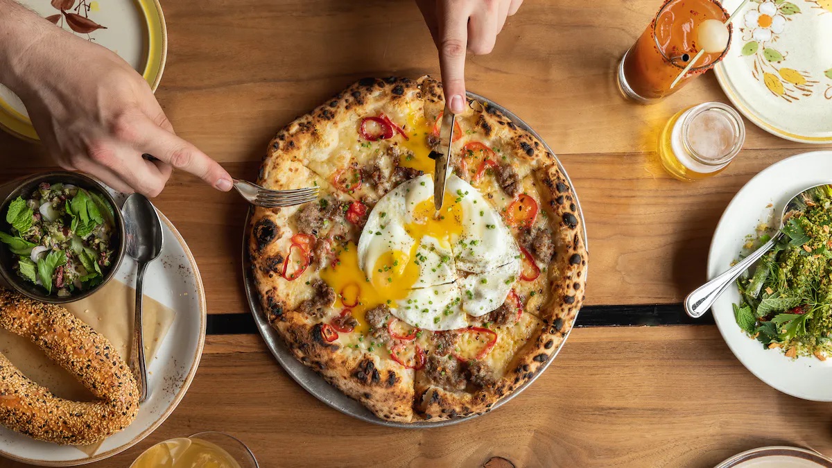 A person cuts a pizza with a fried egg on top of it