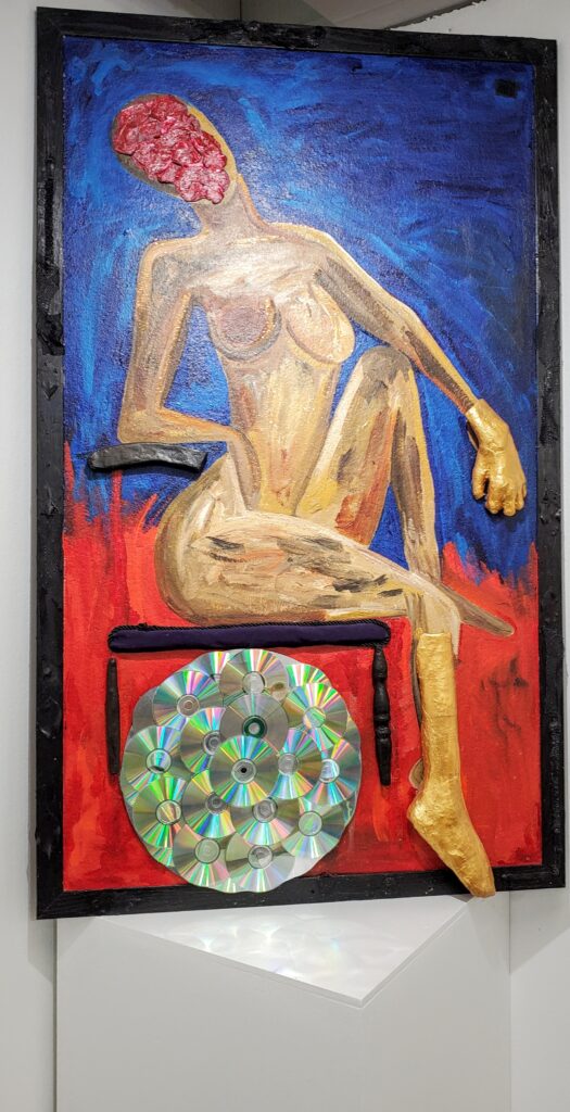A painting of a nude woman sitting on a chair. Instead of a face, she has blobby red paint. Below her is a collage of glittering CDs.