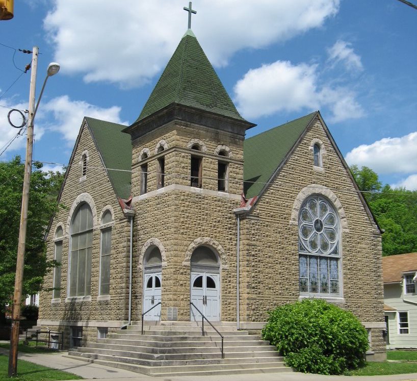 A historic church with a green steeple, a light brown stone exterior, and stained glass windows.