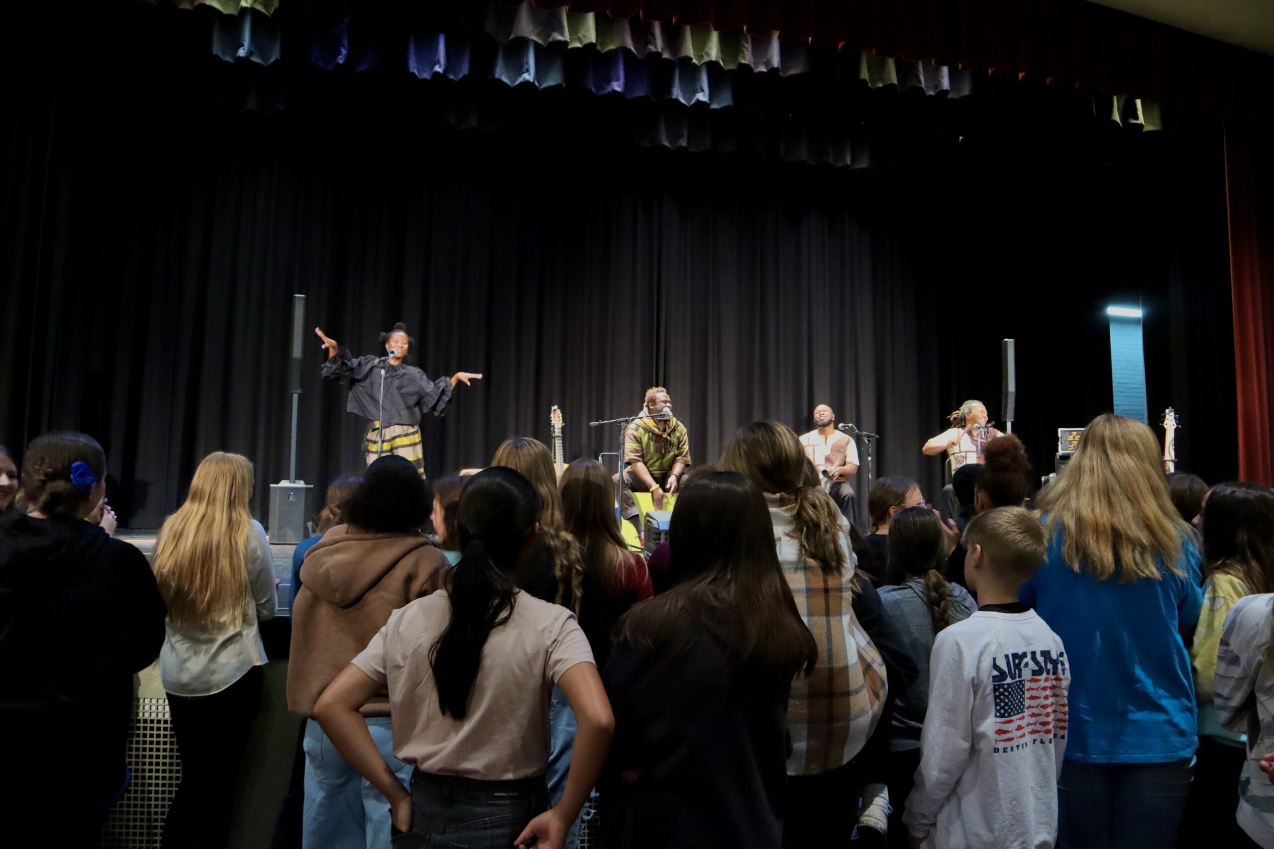 A band performs to a group of middle school students in a gynamsium.