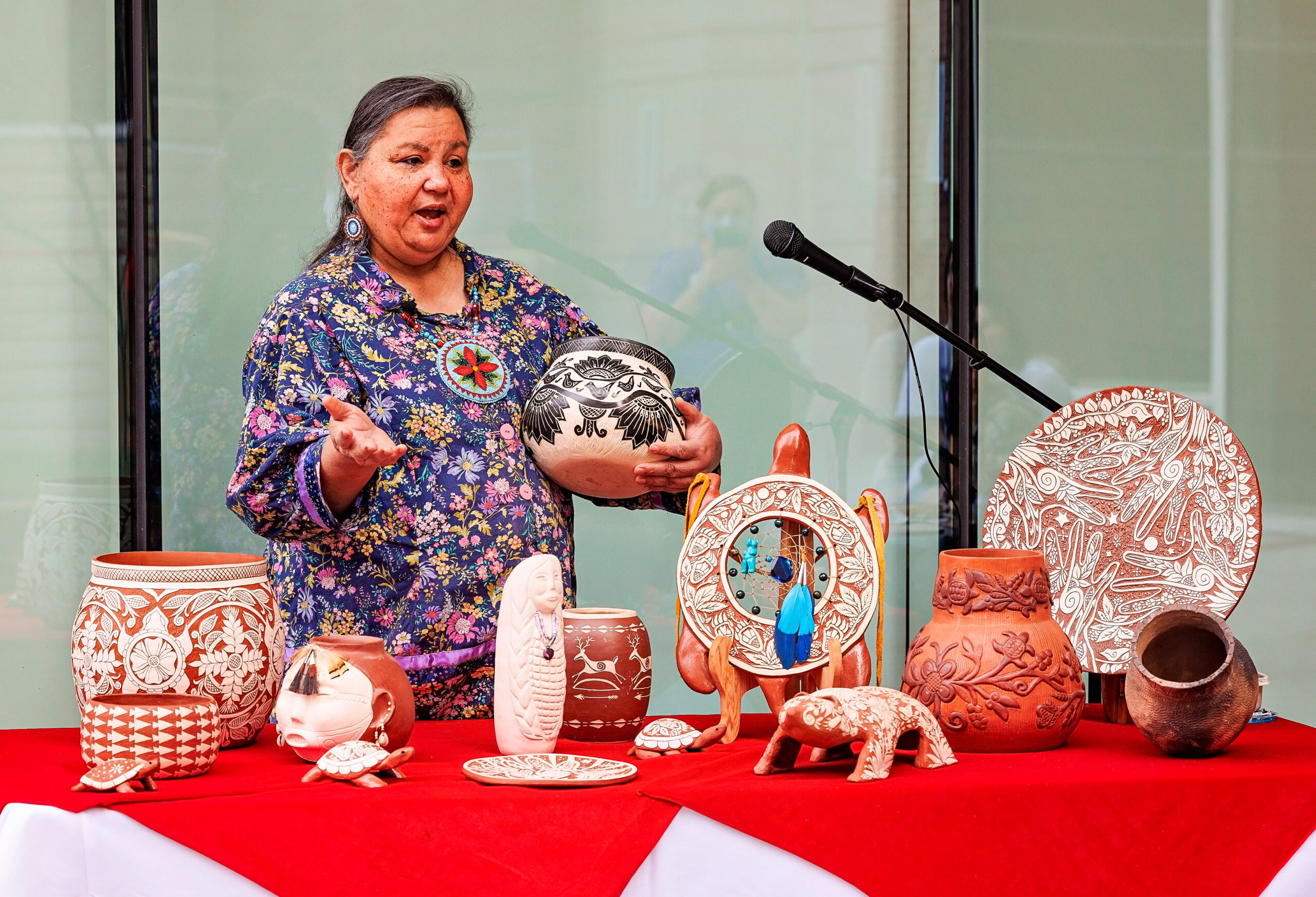 A woman of medium skin tone shows off a colorful assortment of Native pottery.