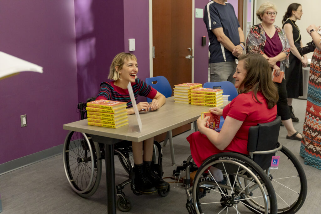 Two women in wheelchairs talking with books.
