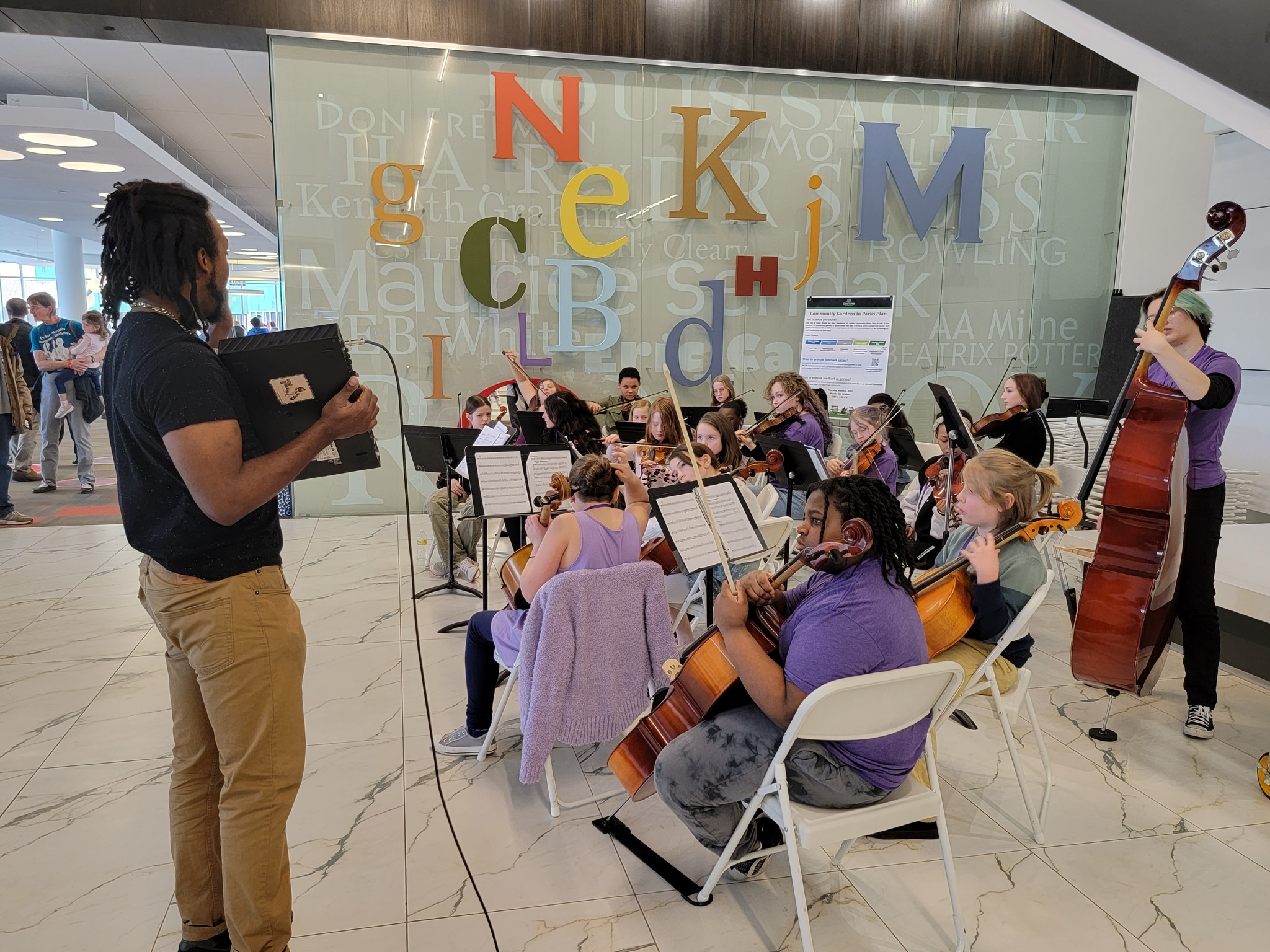 A man with dark skin holds a screen up for a group of young musicians with instruments.