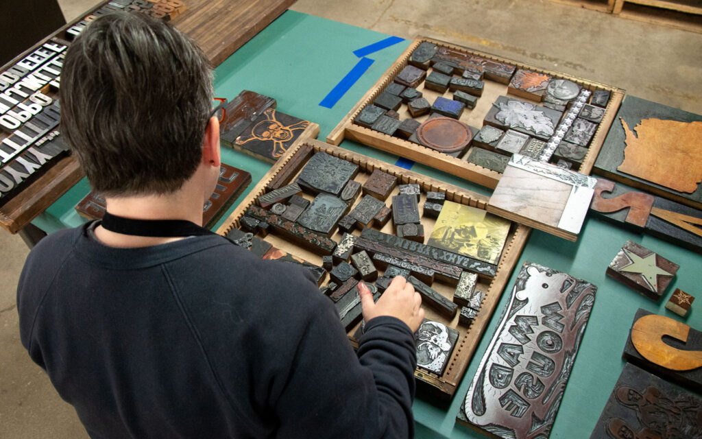 A person, seen from the back, looks at a wide selection of wood blocks arranged in wooden trays.