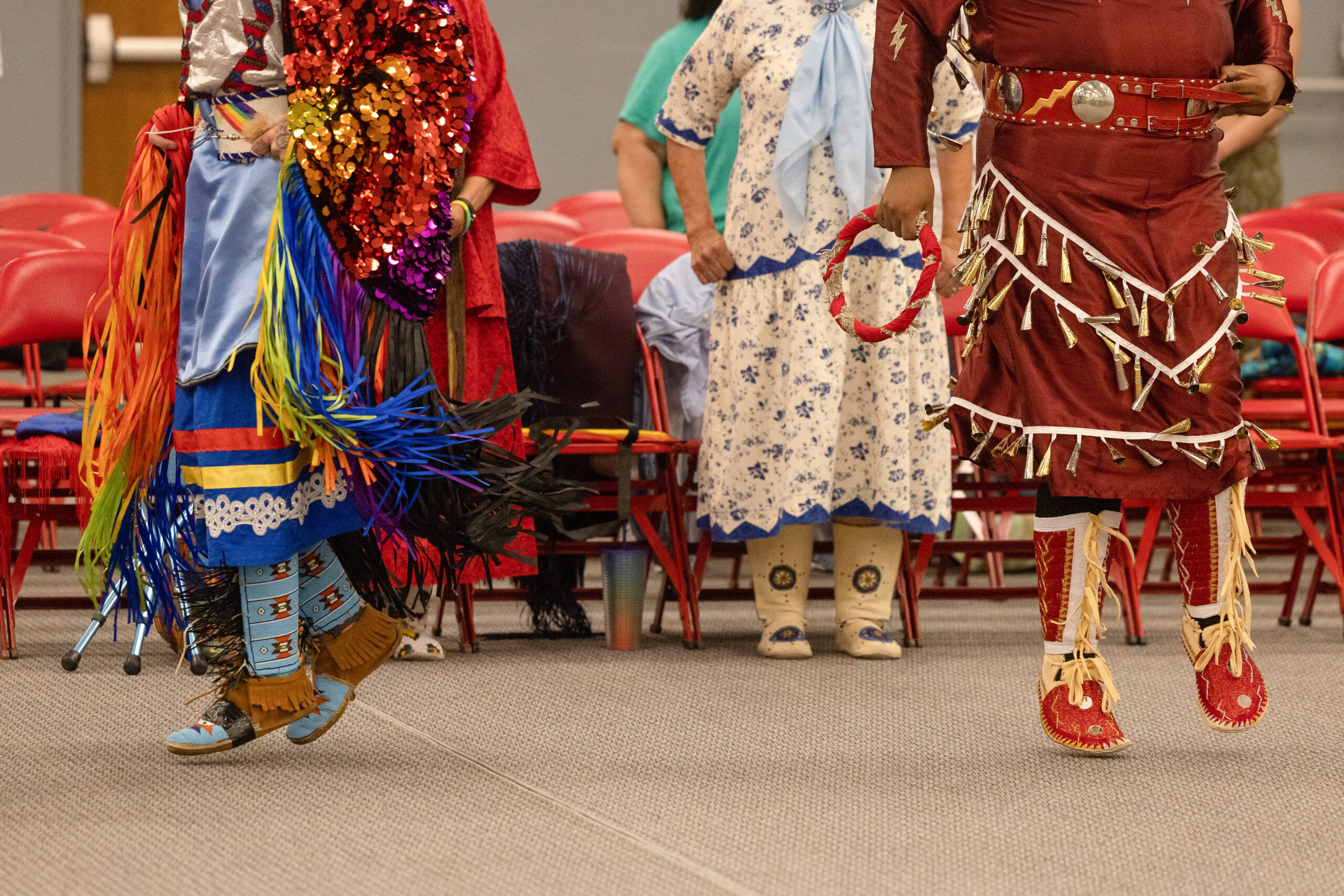 A ground-level shot of three people in colorful regalia dancing; their faces are not visible.