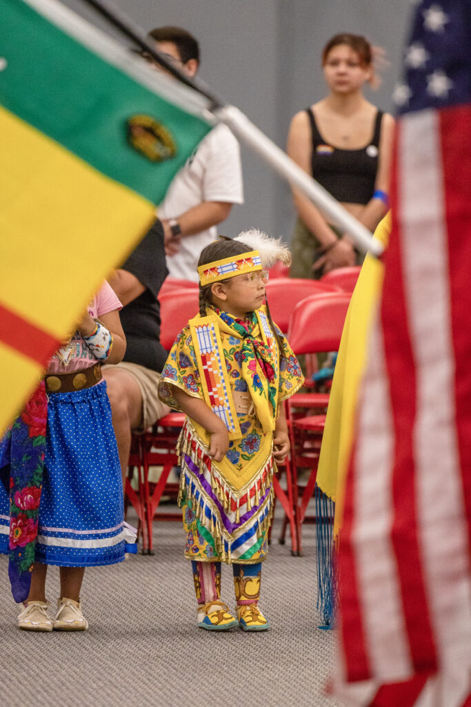 A young person of medium light skin tone wear yellow patterned regalia during a powwow gathering.