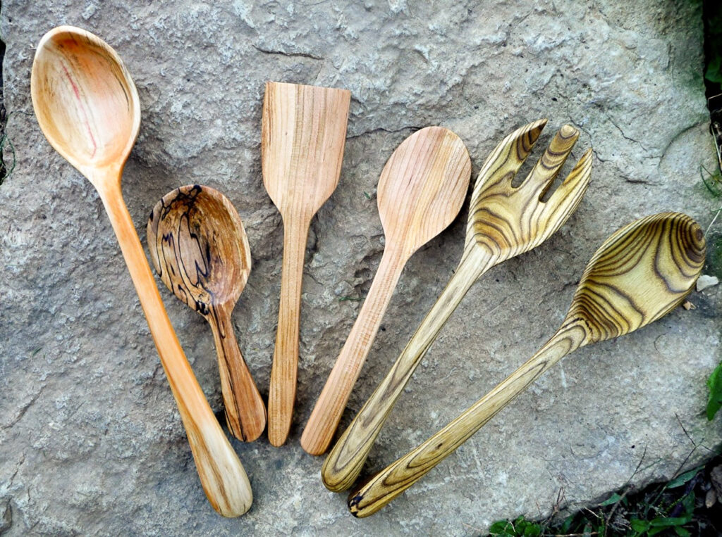 Six wooden spoons of varying shapes and sizes rest on a rock.