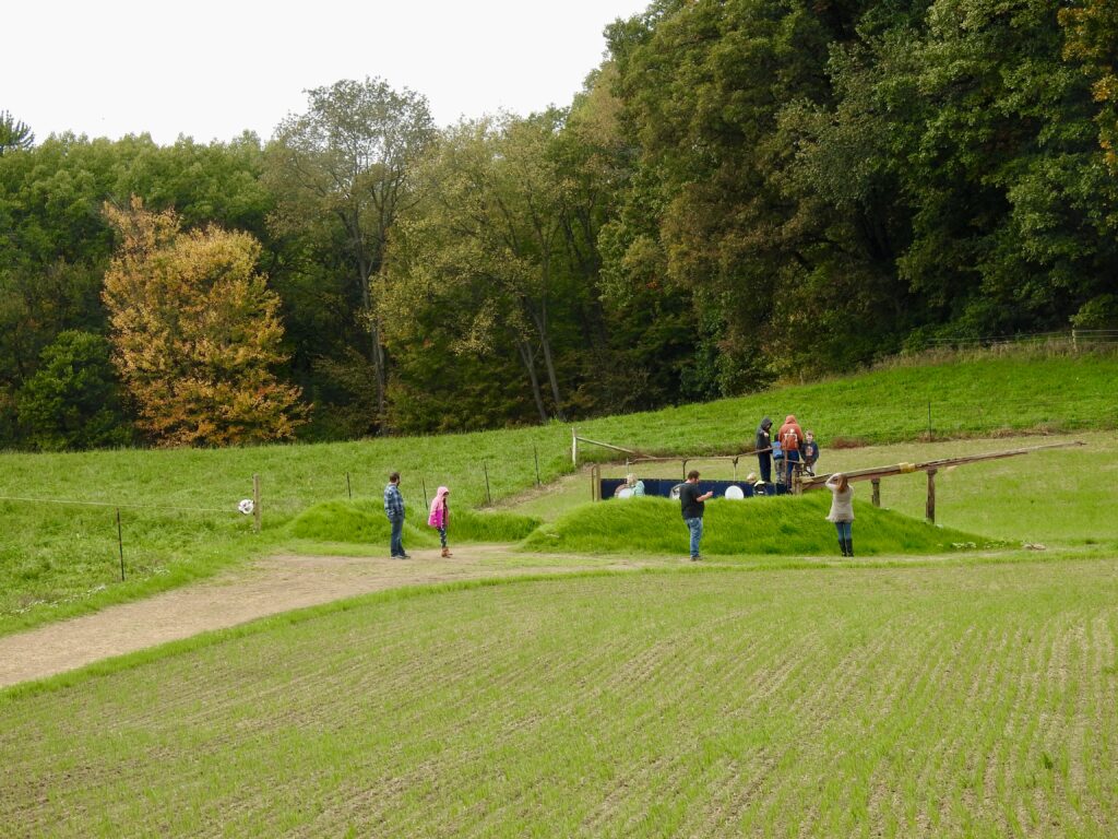 People observe an ark-like outdoor artwork installation on a large farmland.